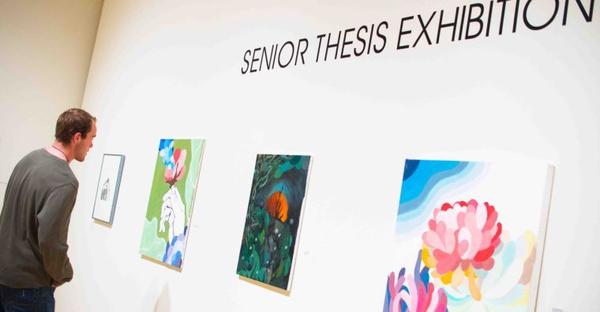 Student views paintings at senior thesis art exhibition