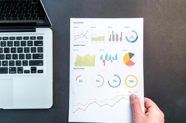 Person holding a paper with analytics next to a laptop. seo vs ppc. Person holding a paper with analytics next to a laptop. seo vs ppc.