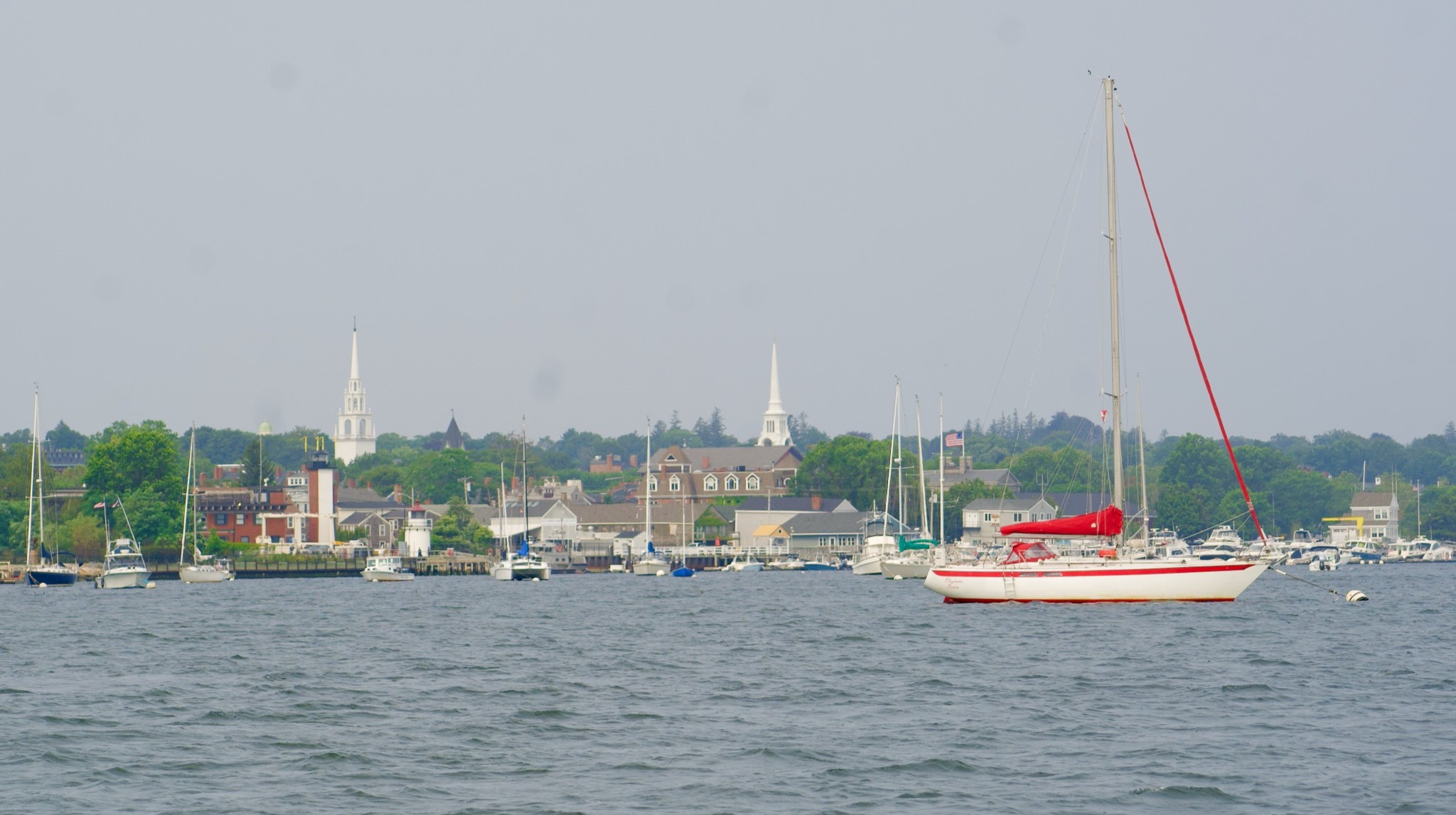 Red and white sailboat on the water, with docks and white steeples in the background Red and white sailboat on the water, with docks and white steeples in the background