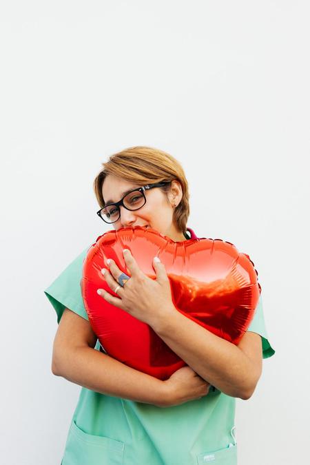 Woman wearing scrubs hugging a heart-shaped balloon