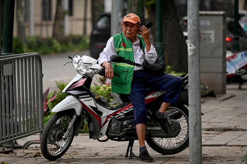 A motorbike taxi driver uses his phone while waiting for a passenger on a street in Hanoi on April 17, 2026