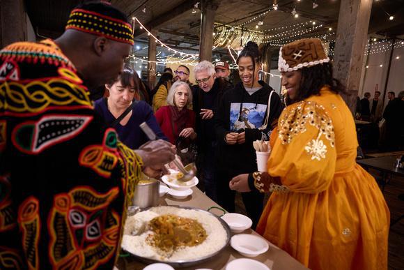 Chef in African robes serves food to line of people