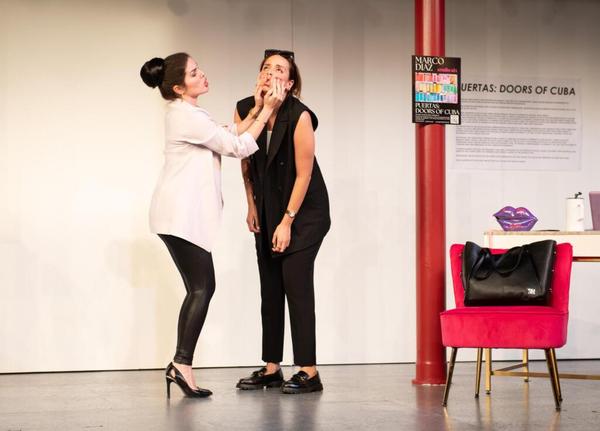A stylish woman squeezes another woman's face next in a white-walled gallery