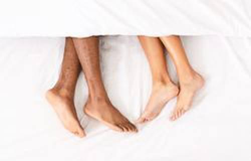 Two pairs of feet in bed sticking out of the sheets