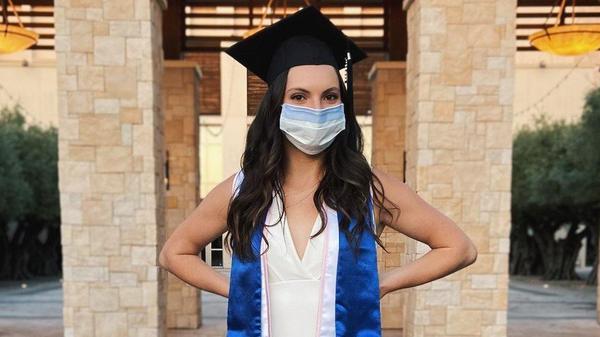 Giulia stands posed in her graduation stole, graduation cap, with a face mask to portray graduating during the COVID-19 global pandemic