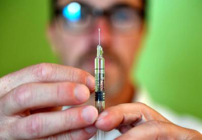 Out of focus photo of a man holding a vaccine syringe up for the camera to see