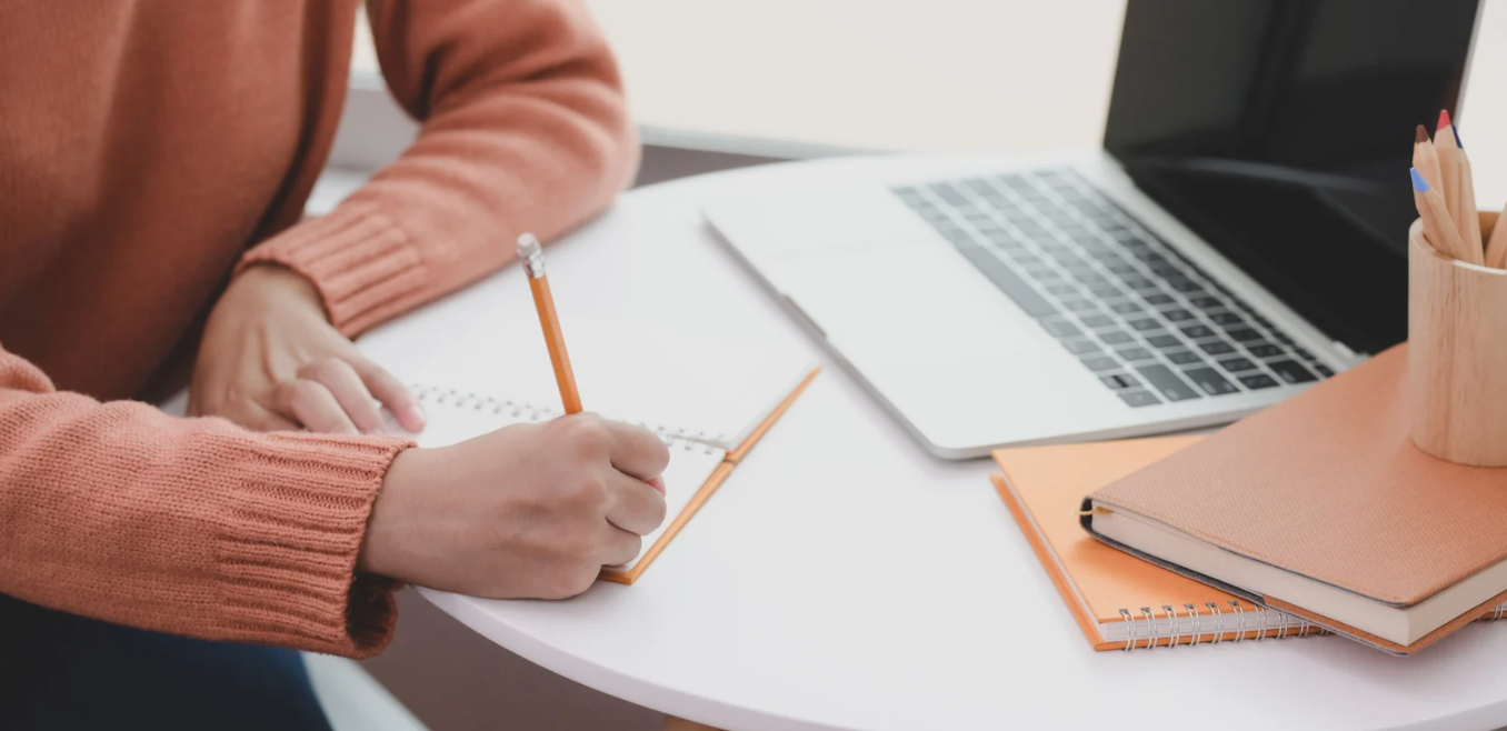 writer holding a pencil next to computer