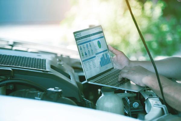 A person looking at a laptop with data while working under the hood of a car