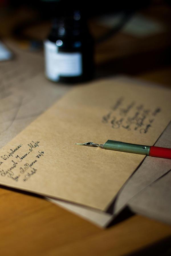 An addressed brown envelope is seen, with a red and gold fountain pen on top, and a bottle of ink to the side.