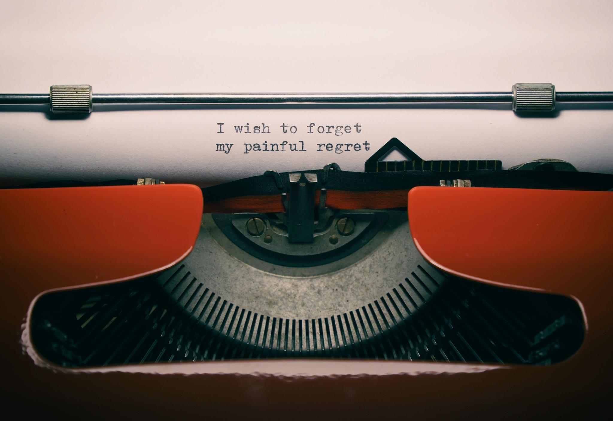 A typewriter is seen, on which, black text on white paper states: I wish to forget my painful regret