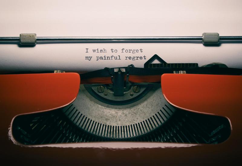 A typewriter is seen, on which, black text on white paper states: I wish to forget my painful regret