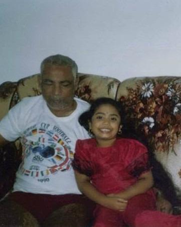 A cropped photo from the author's childhood is seen. Dindial Goorahoo, a brown man with grey hair, is seen in a tee shirt, beside Krystal Kavita Jagoo, a young brown girl, who smiles widely. They are seated on a floral couch.