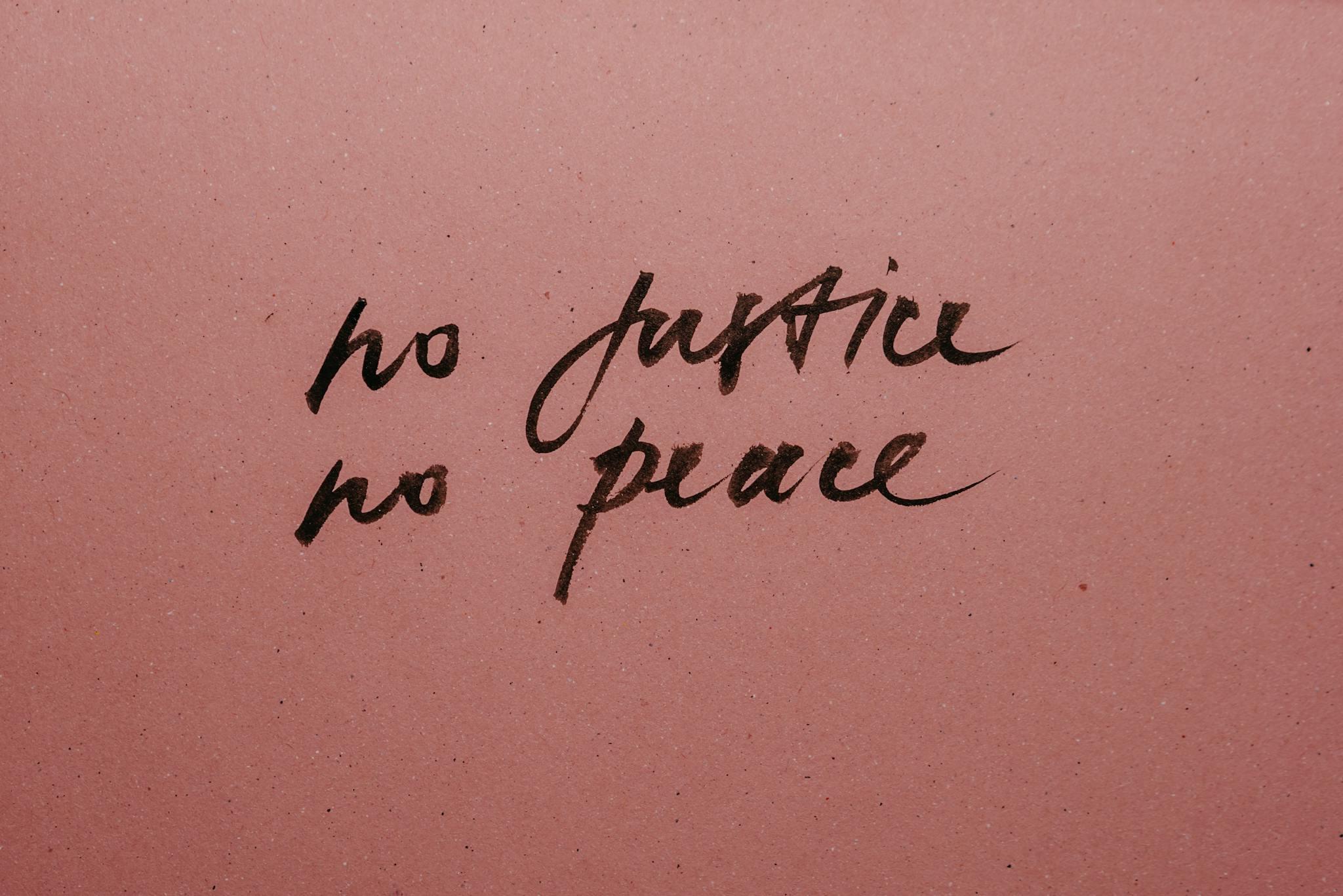 Against a pink background, brown cursive writing states, "no justice no peace"