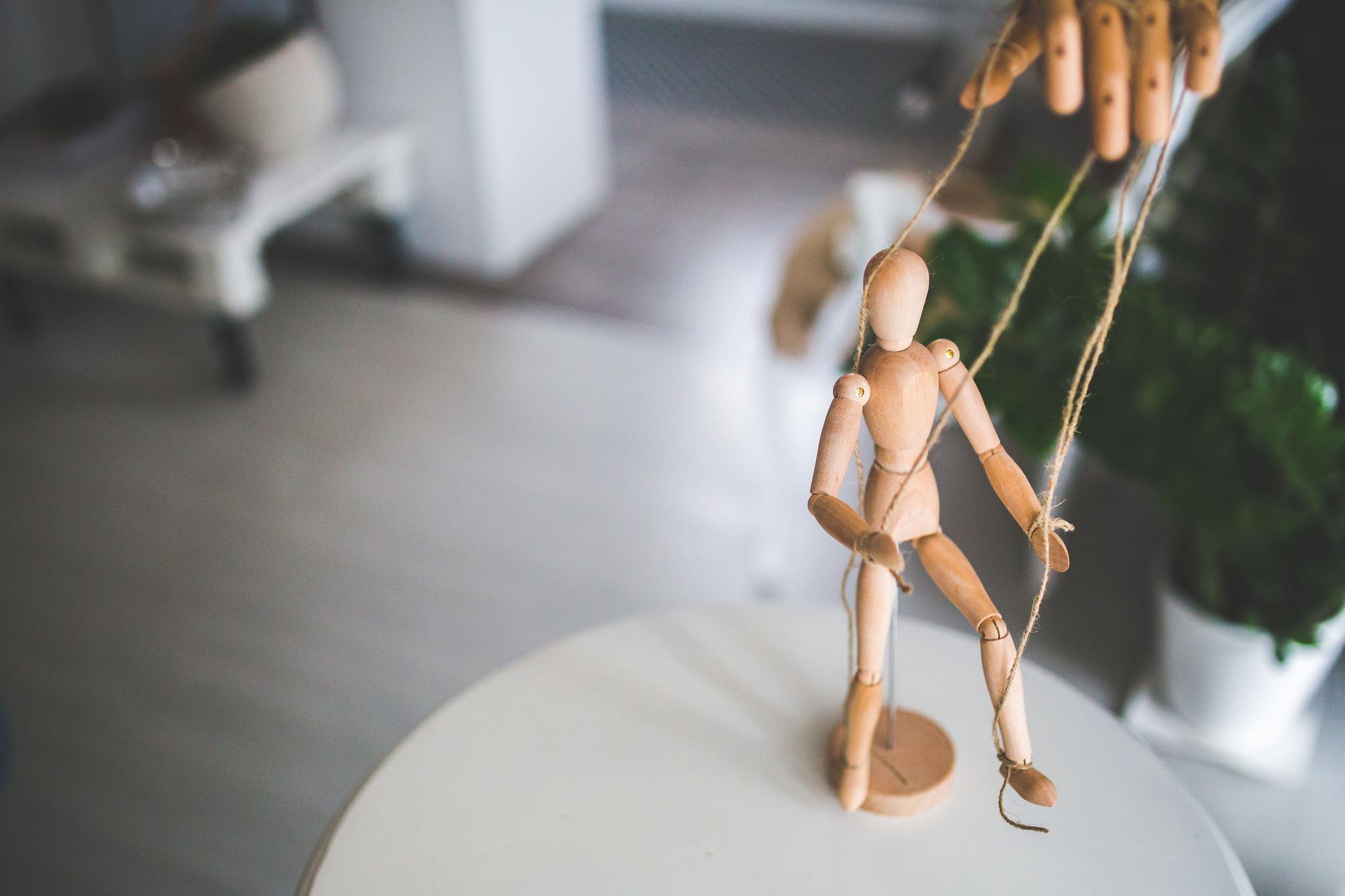A wooden puppet is seen manipulated by fingers.