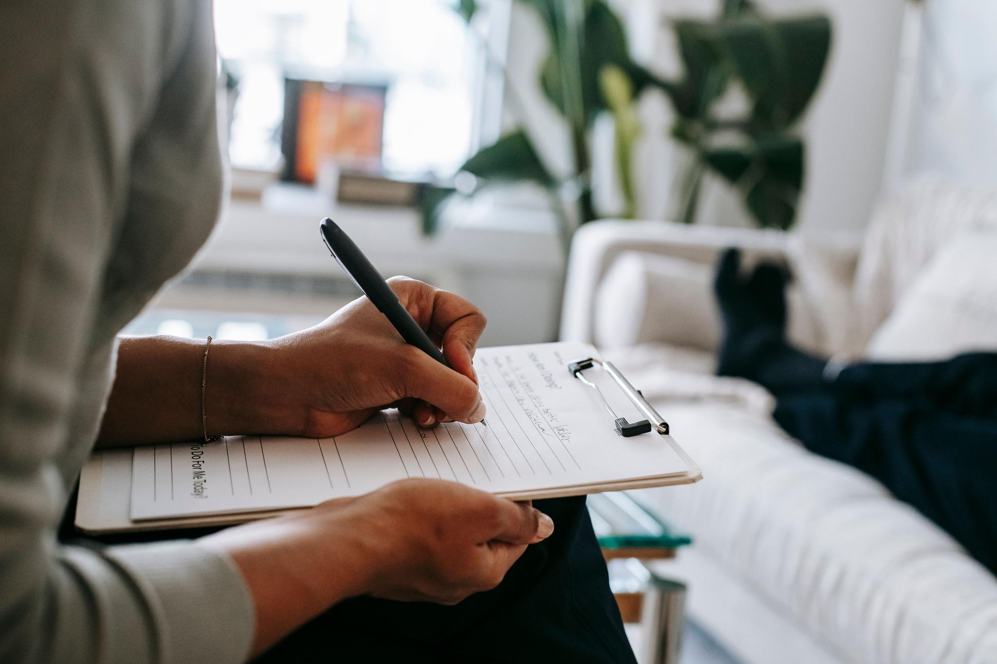 Ethnic mental health professional is seen writing on a clipboard in a well-lit room.