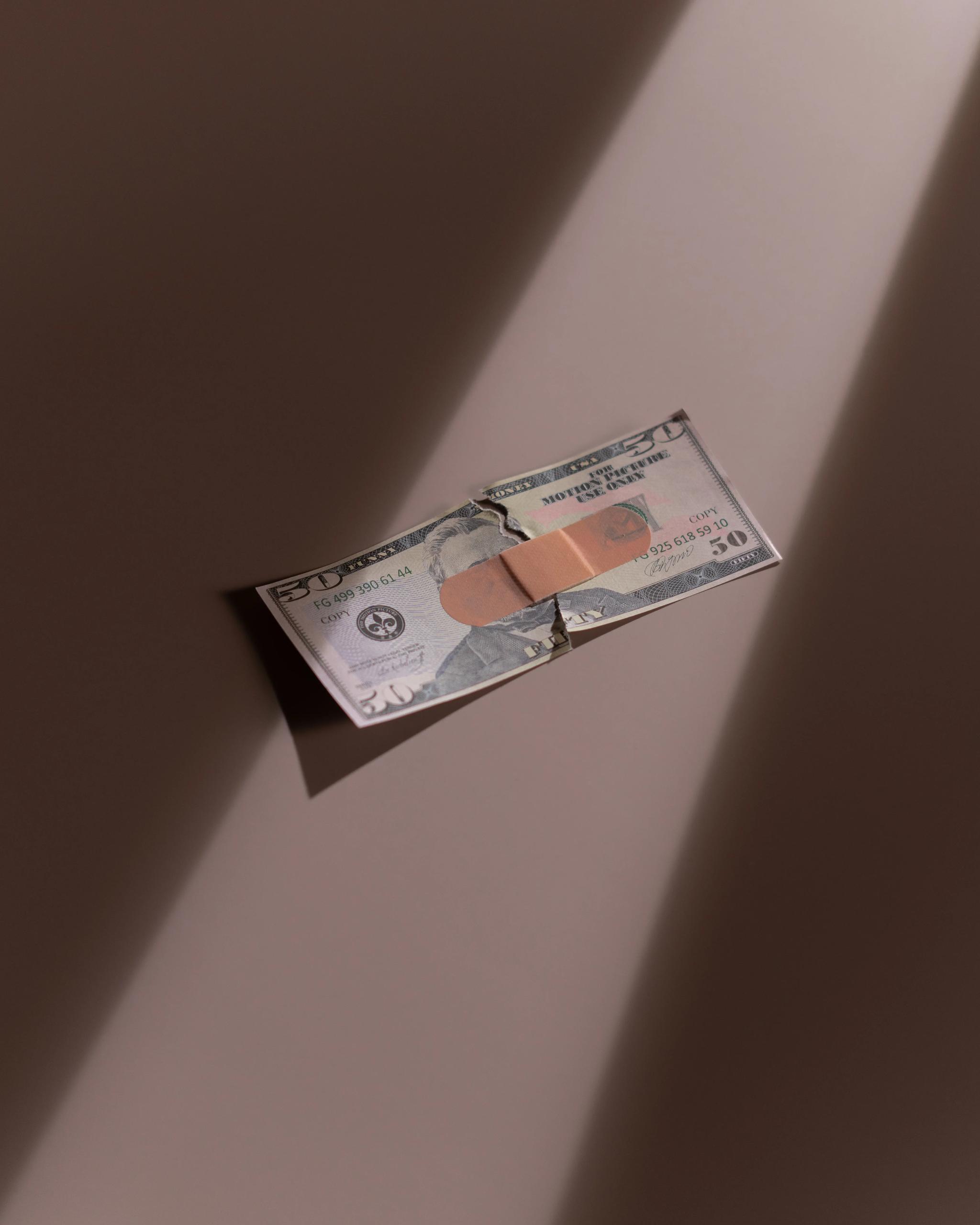 A torn $50 bill is seen with a band-aid holding it together.