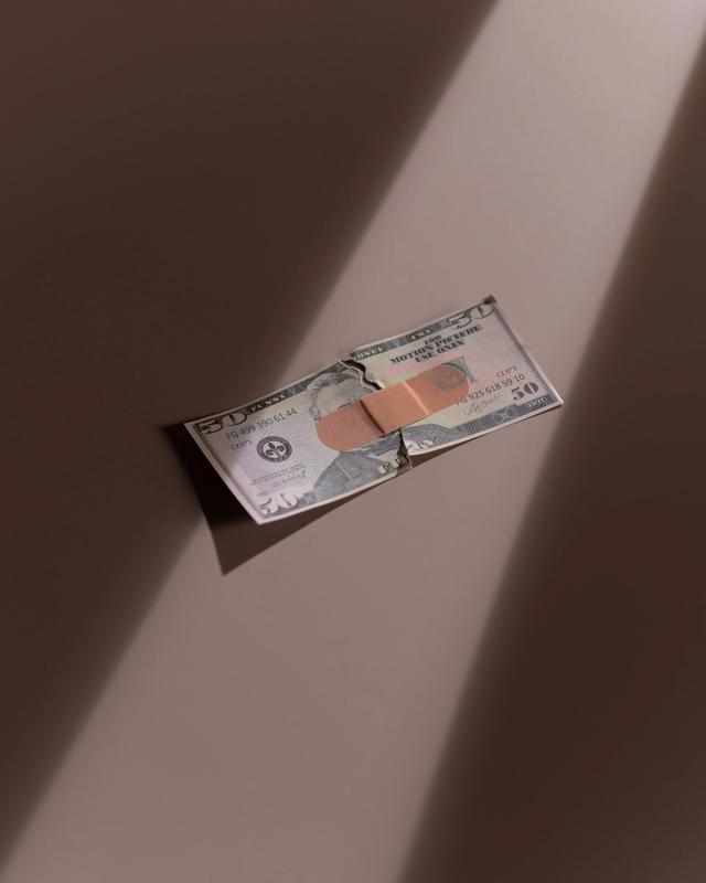 A torn $50 bill is seen with a band-aid holding it together.