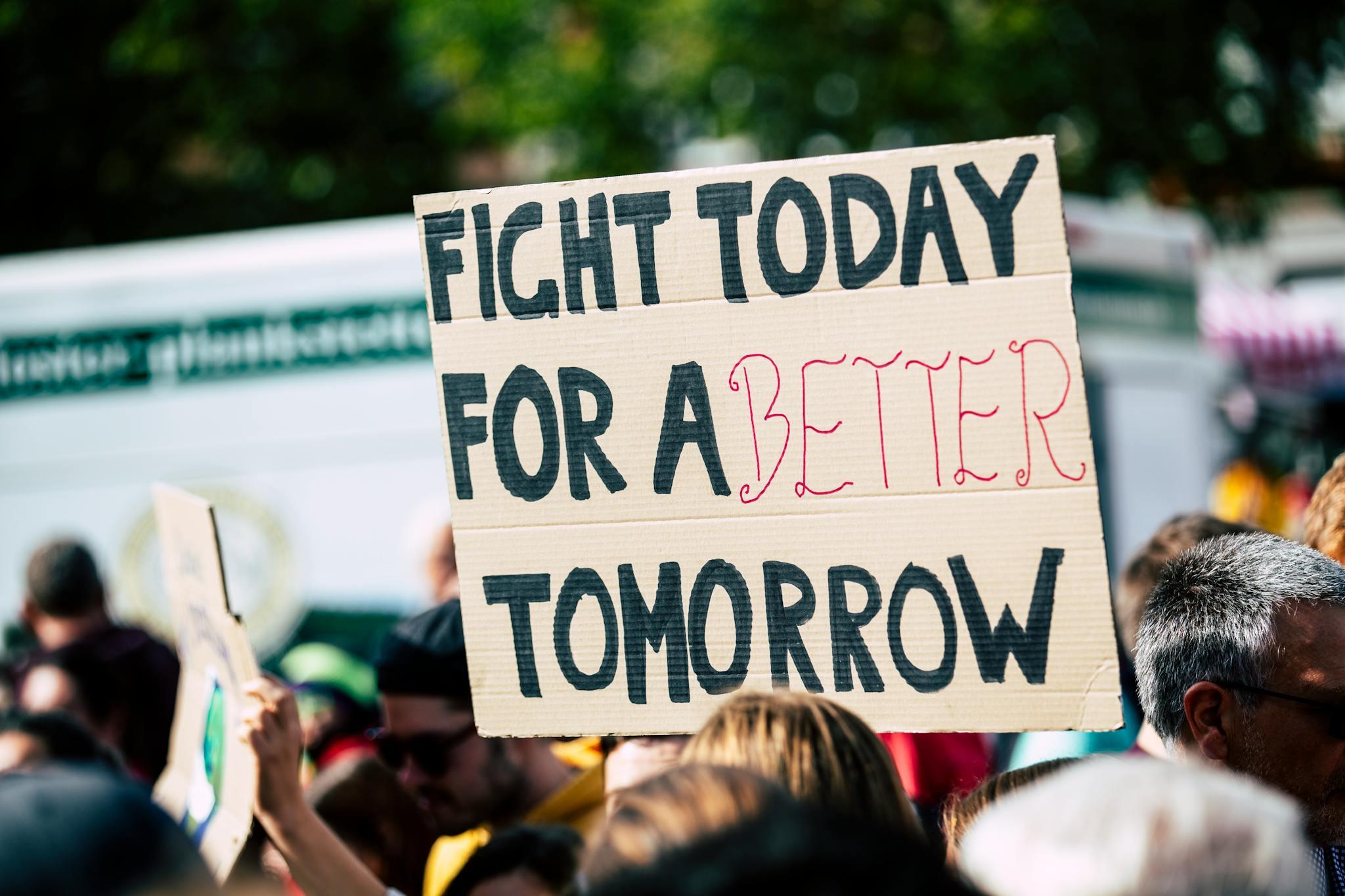 A protest is seen, with a sign, which states, "FIGHT TODAY FOR A BETTER TOMORROW"