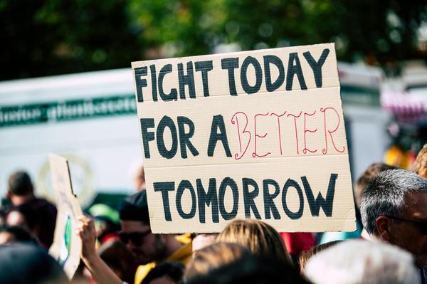A protest is seen, with a sign, which states, "FIGHT TODAY FOR A BETTER TOMORROW"