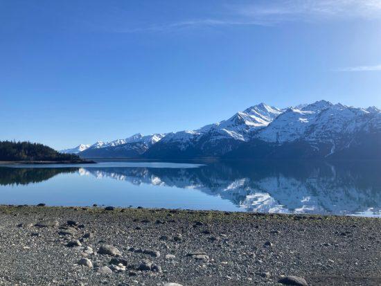 Chilkat Inlet on a flat calm day, with blue sky and snow-covered mountains reflected in its glassy surface