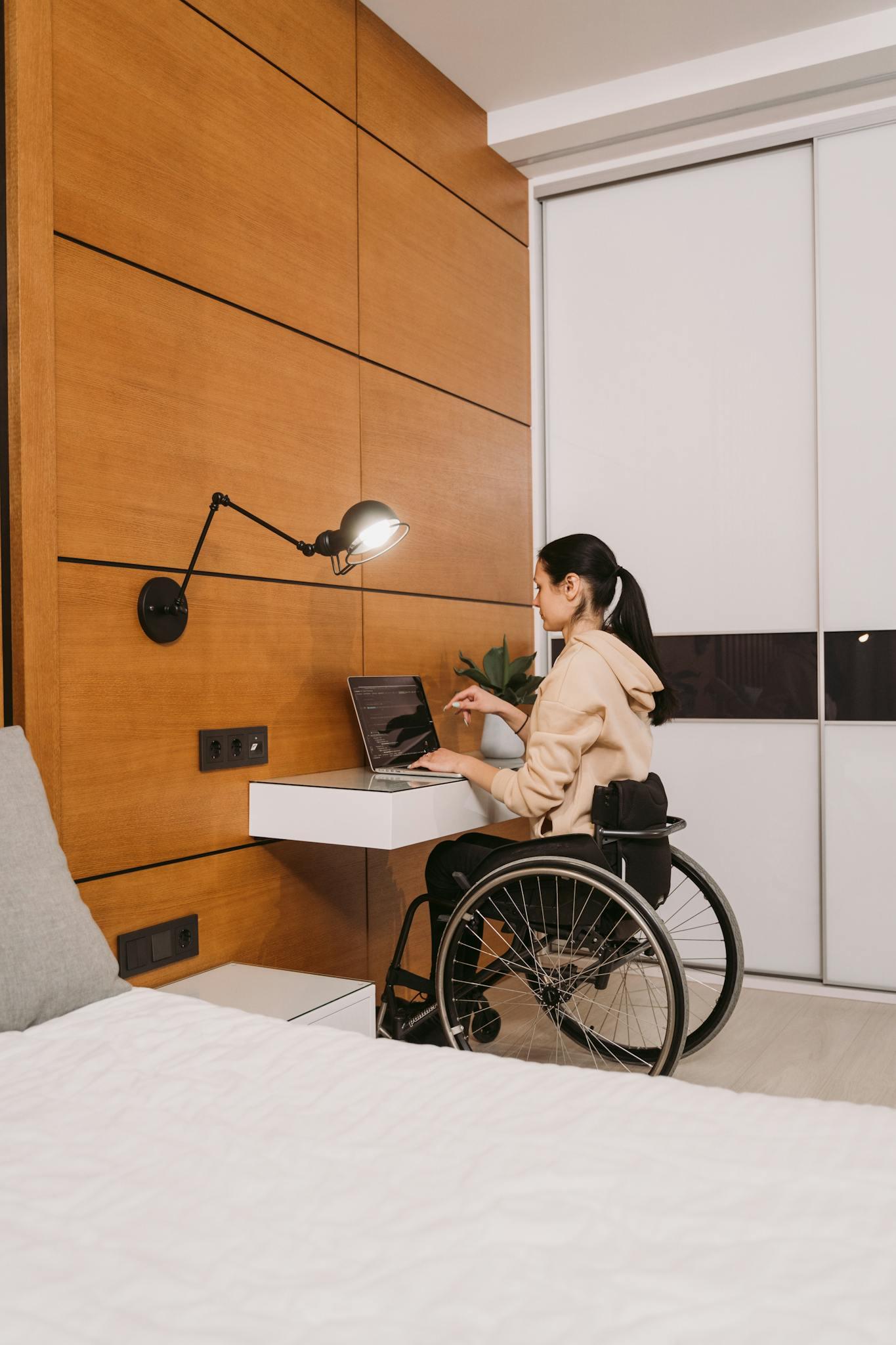 A woman sitting in a wheelchair at a desk and typing on a laptop