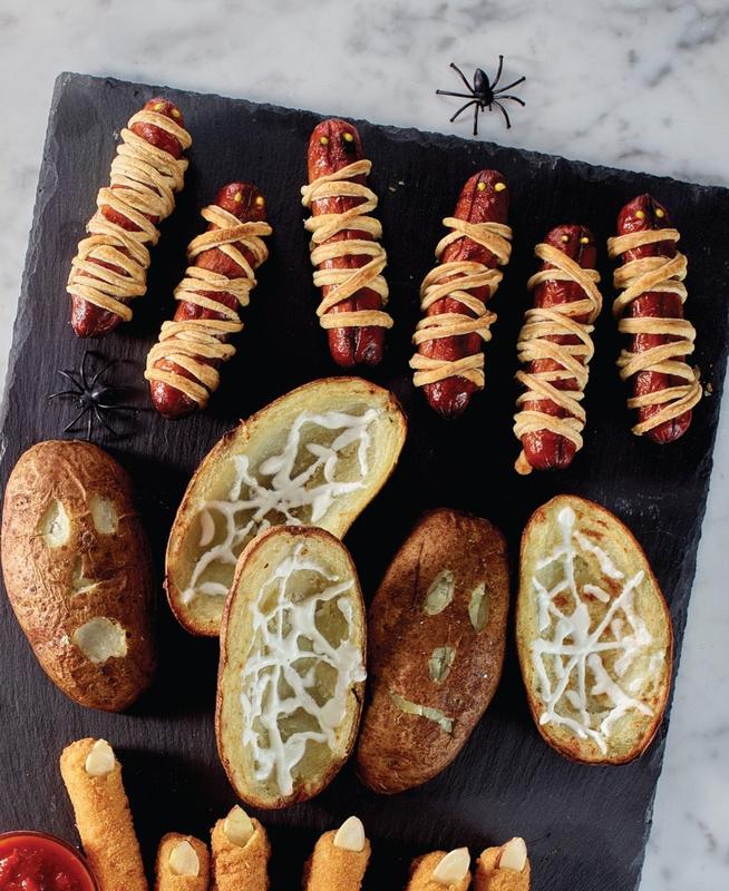 A charcuterie board full of Halloween appetizers like hot dog mummies, spiderweb potato skins and mozzarella cheese fingers