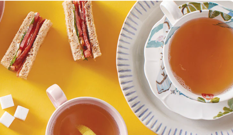 Tea in a porcelain mug alongside small sandwiches and sugar cubes.