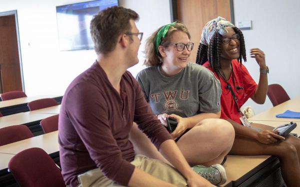 Members of TWU's Smash Brother's Alliance sit on top of a table in a repurposed classroom during the Smash Social social gaming event held at TWU.