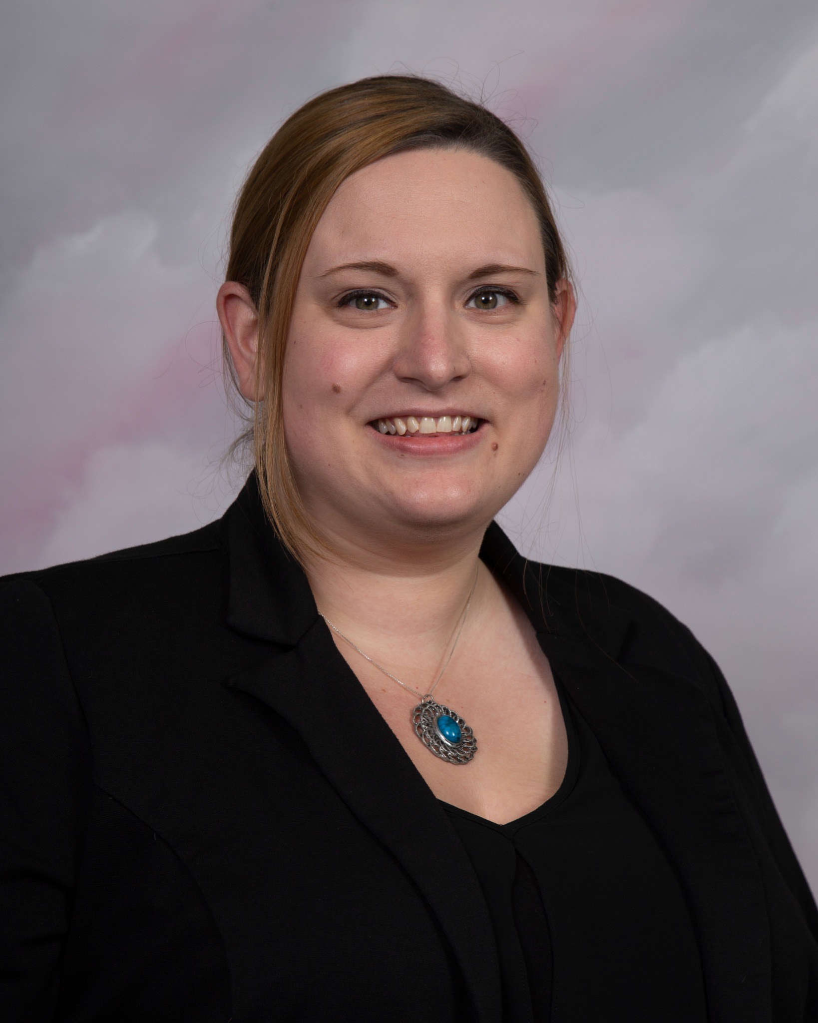 A smiling white woman, Katie Monfet, with her hair pulled back and wearing a black blazer and a pendant necklace. A smiling white woman, Katie Monfet, with her hair pulled back and wearing a black blazer and a pendant necklace.