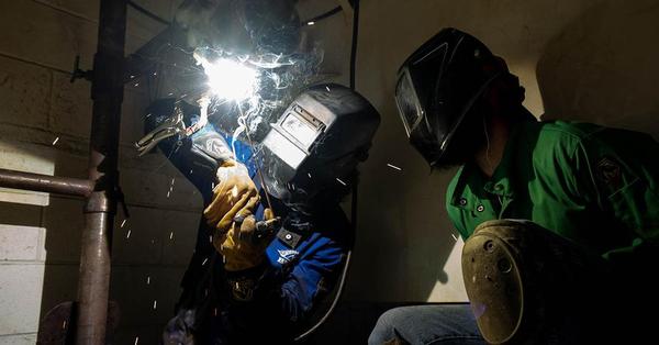 Two people in protective gear welding a metal object.