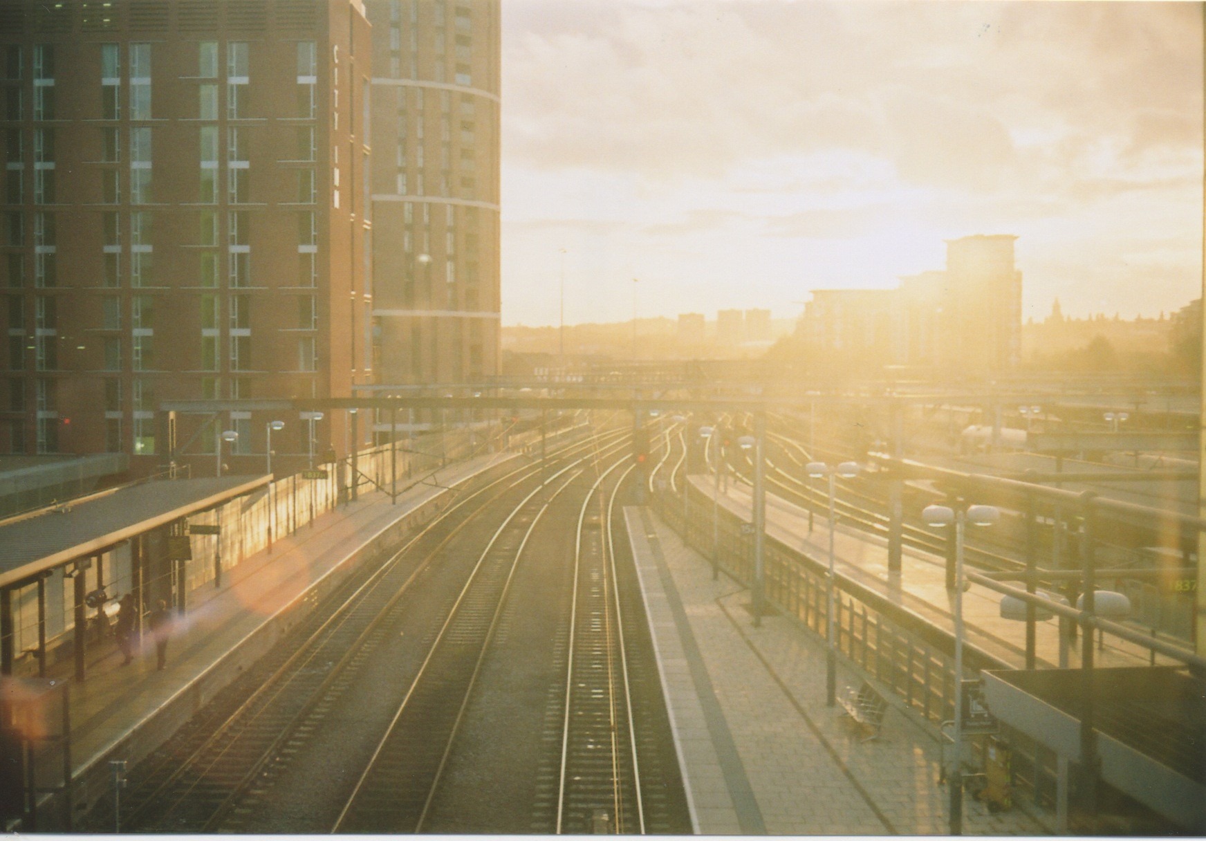 Leeds city train station railway lines with the run rising/setting in the distance. There is a high-rise building to the left of the tracks.