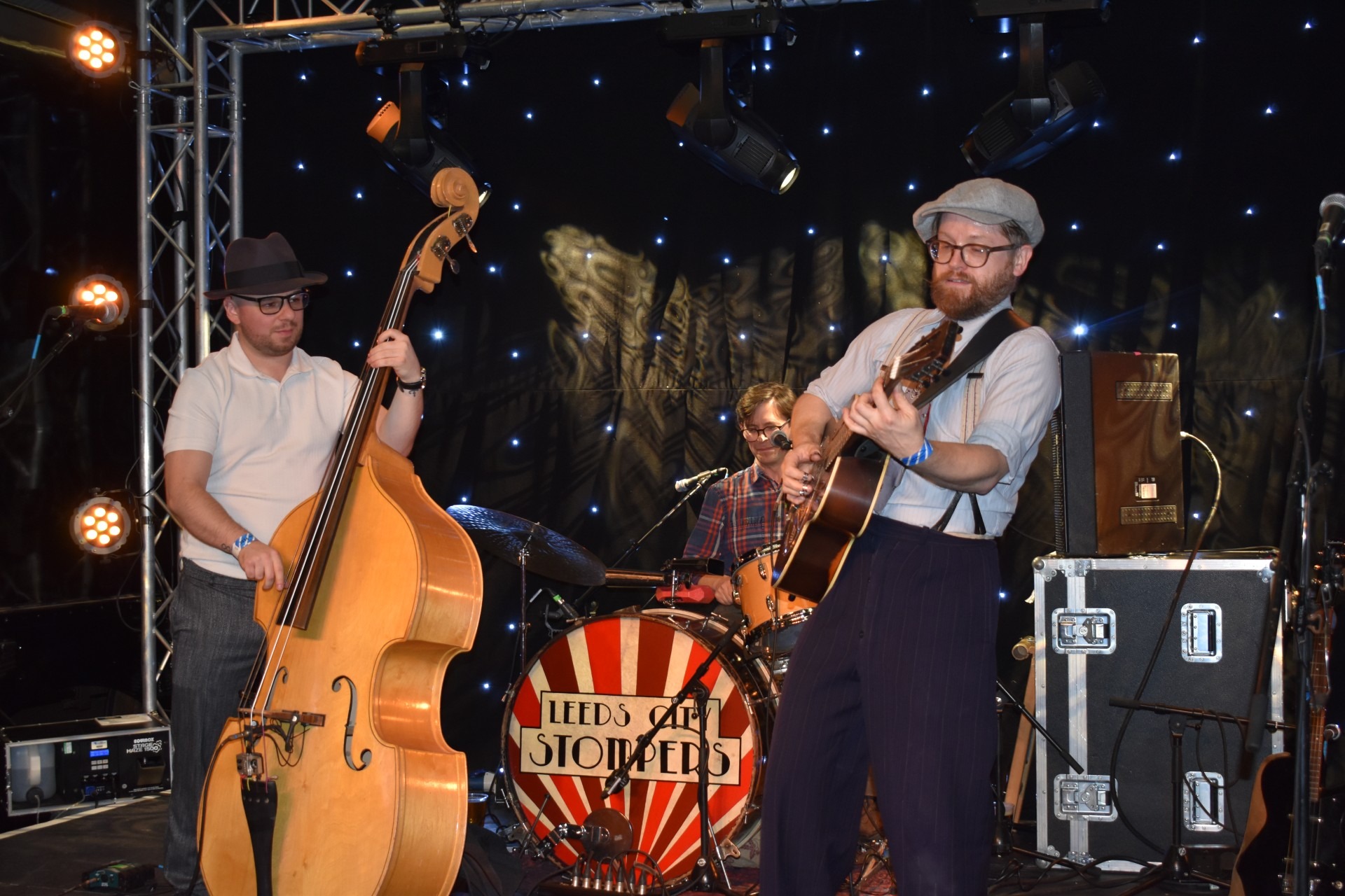 he Leeds City Stompers band performing at Oxenhope station. There is a bass player on the left, the drummer is in the middle at the back of the stage, and the guitarist is positioned on the right