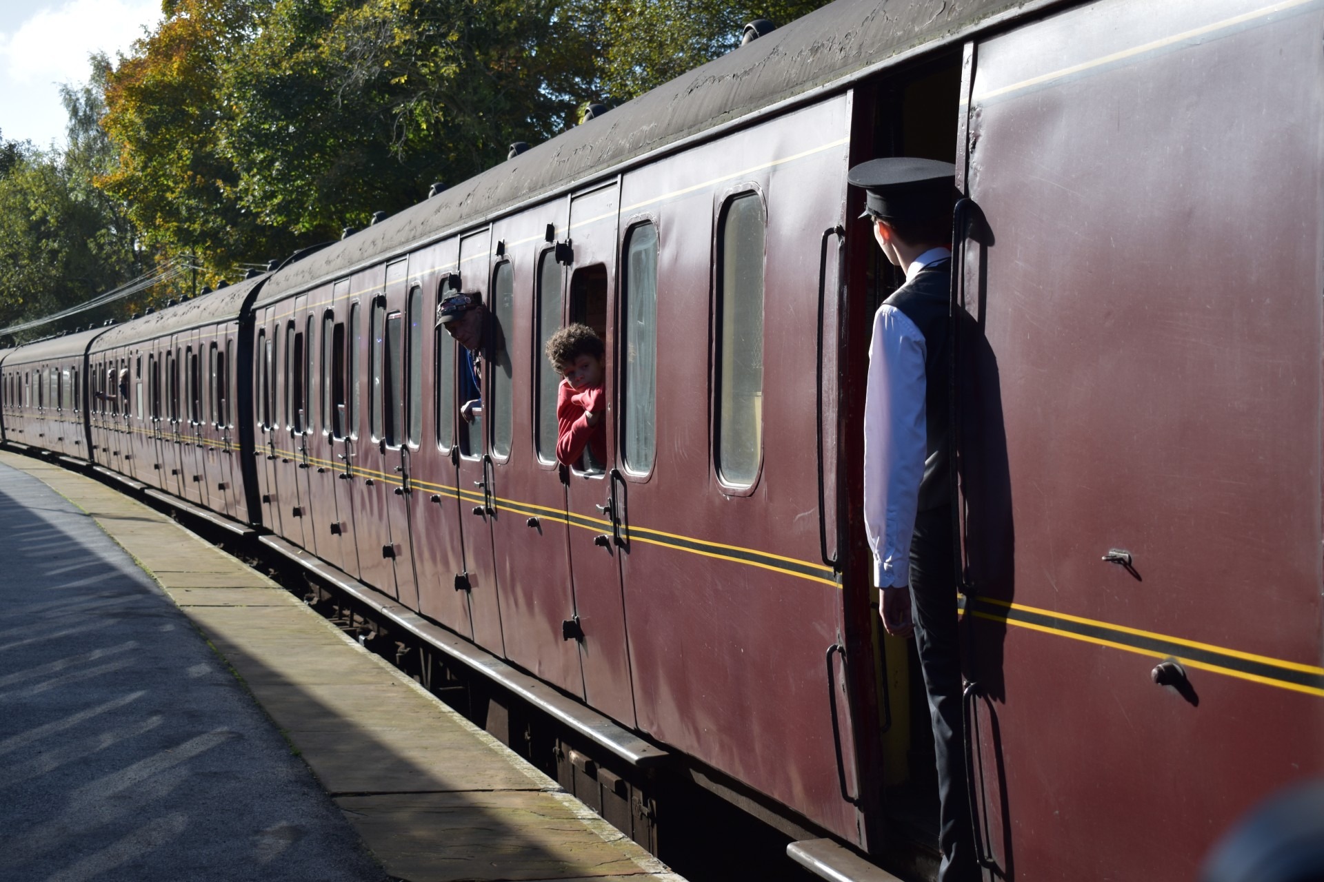 An old, dark red coloured steam train getting ready to depart from Oxenhope station. There are people