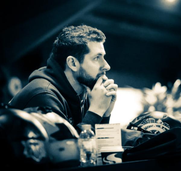 This is a black and white image of a man's side profile. He's looking into the distance with his hands raised to his mouth. He has short hair and a dark beard.