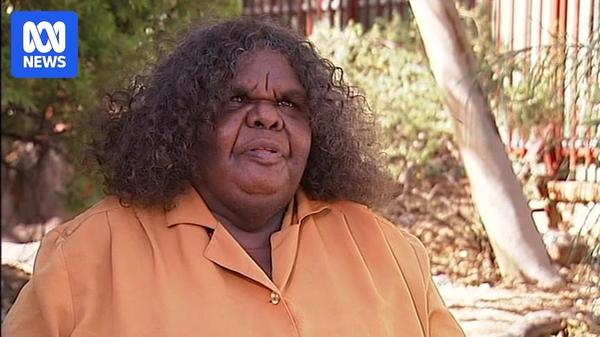A woman with shoulder-length brown curly hair sits outside speaking to someone out of frame
