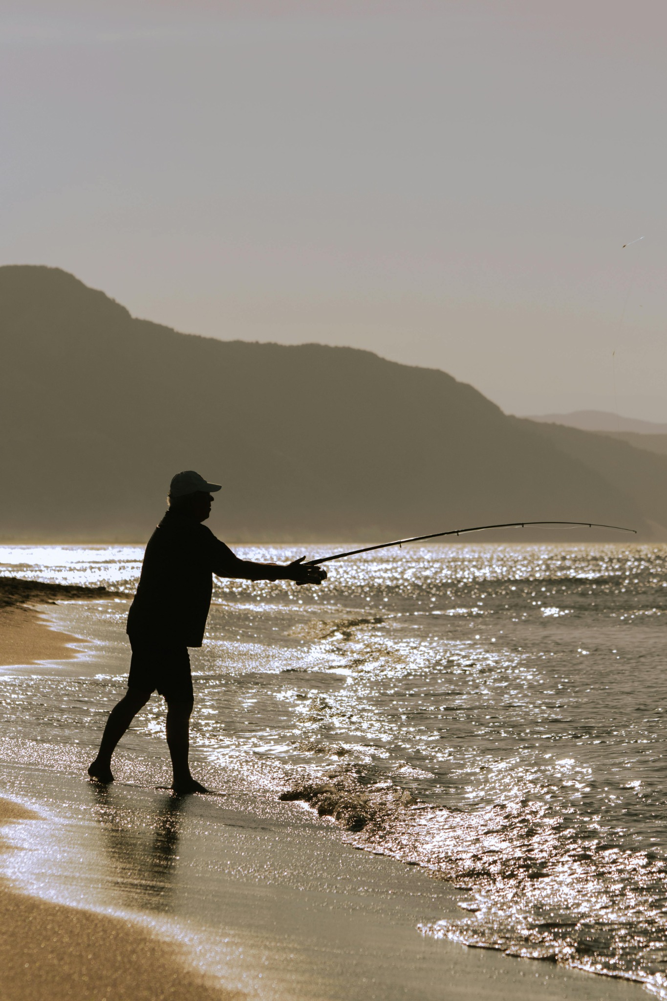 pêcheur à la ligne au bord de la mer avec des montagnes dans le fond