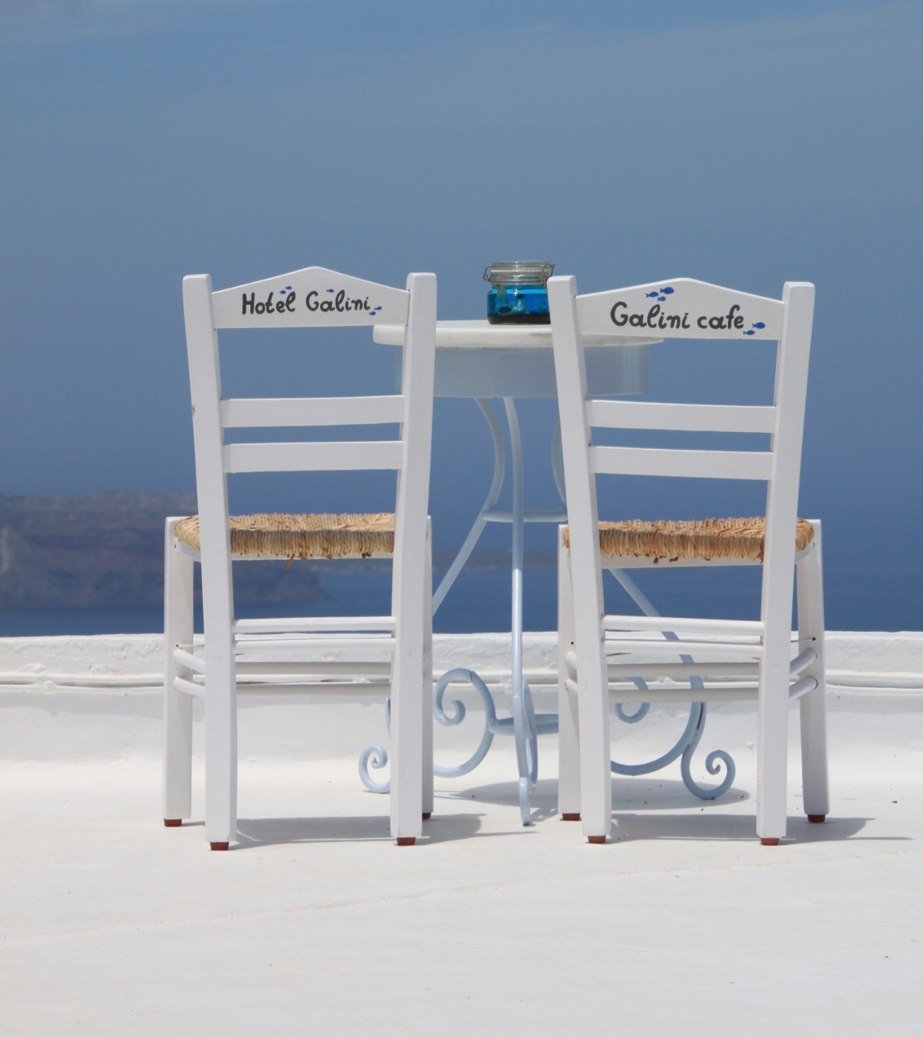 deux chaises blanches en bois sur une terrasse blanche au-dessus de la mer sous un ciel bleu