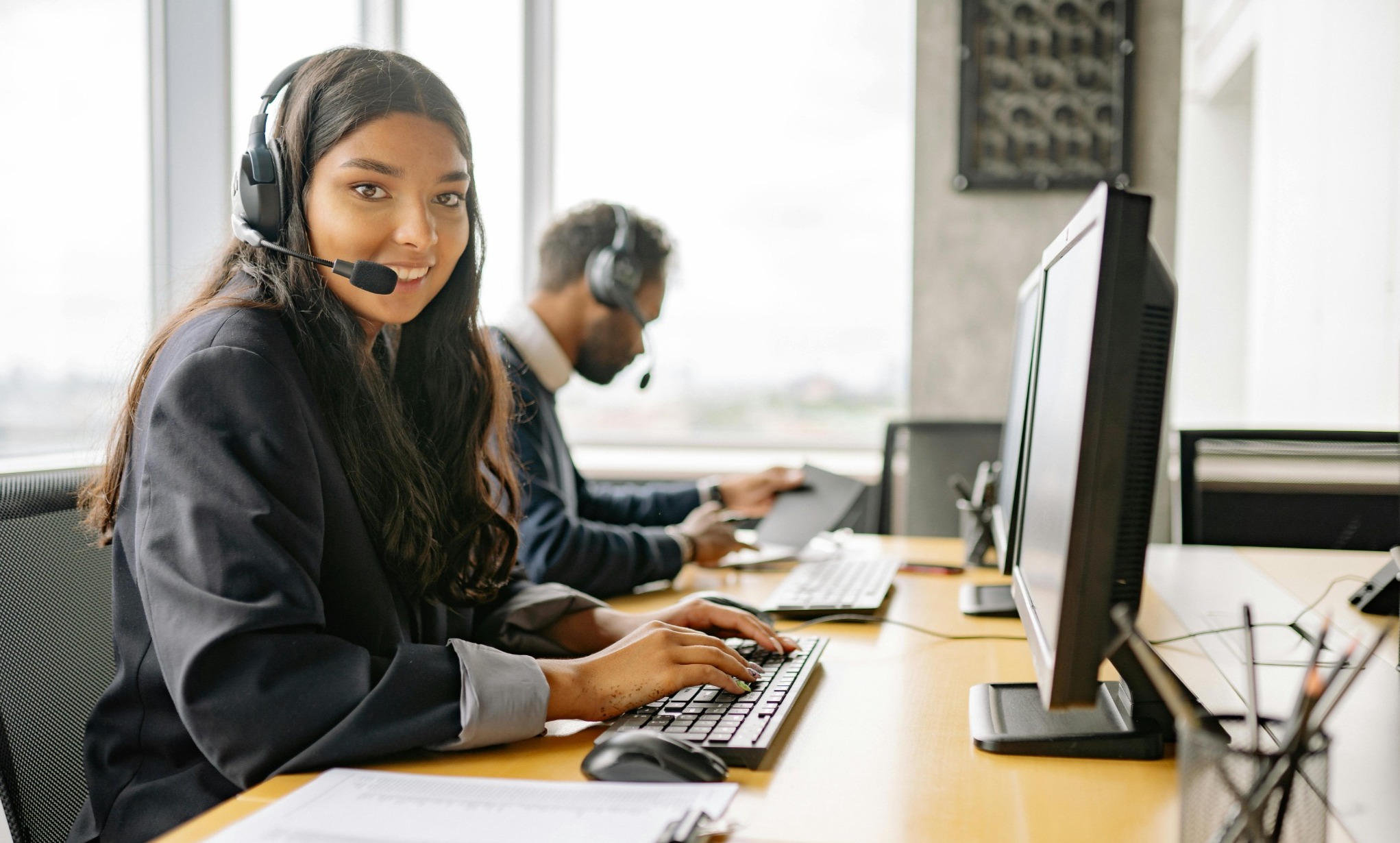 femme souriante dans un bureau, avec un casque de téléphone devant un ordinateur