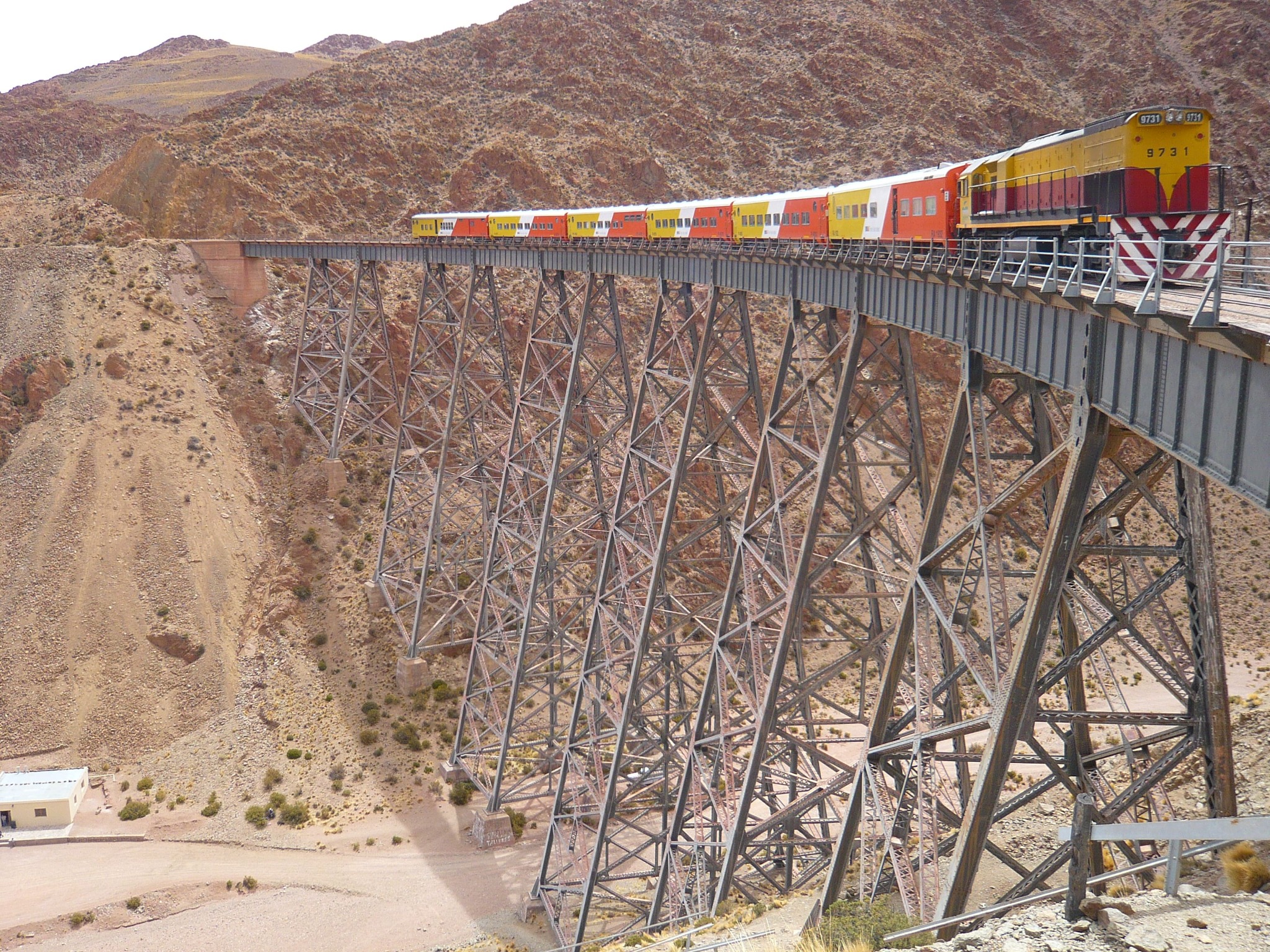 train rouge jaune et blanc qui passe sur un pont très haut entre 2 falaises dans un paysage désertique