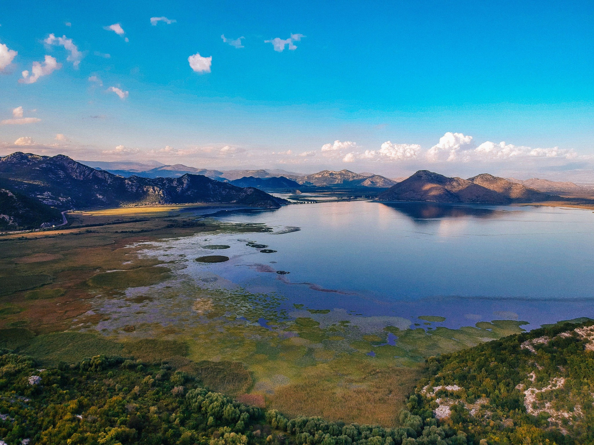 lac entouré de montagnes sous un ciel bleu et quelques nuages dans le fond