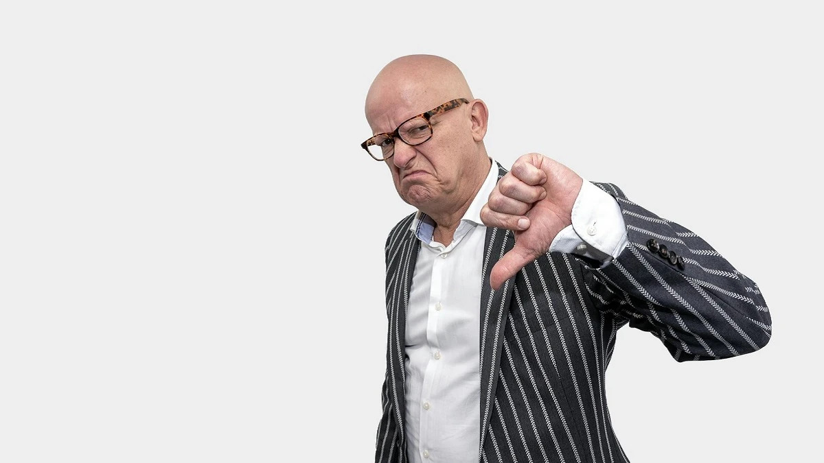 A photo of a grumpy, bald man giving a thumbs down.