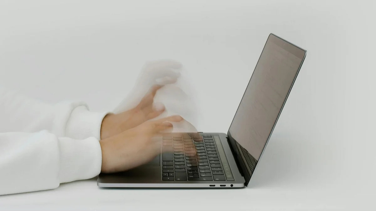 A photo of some hands in a blur as they quickly type at a laptop.