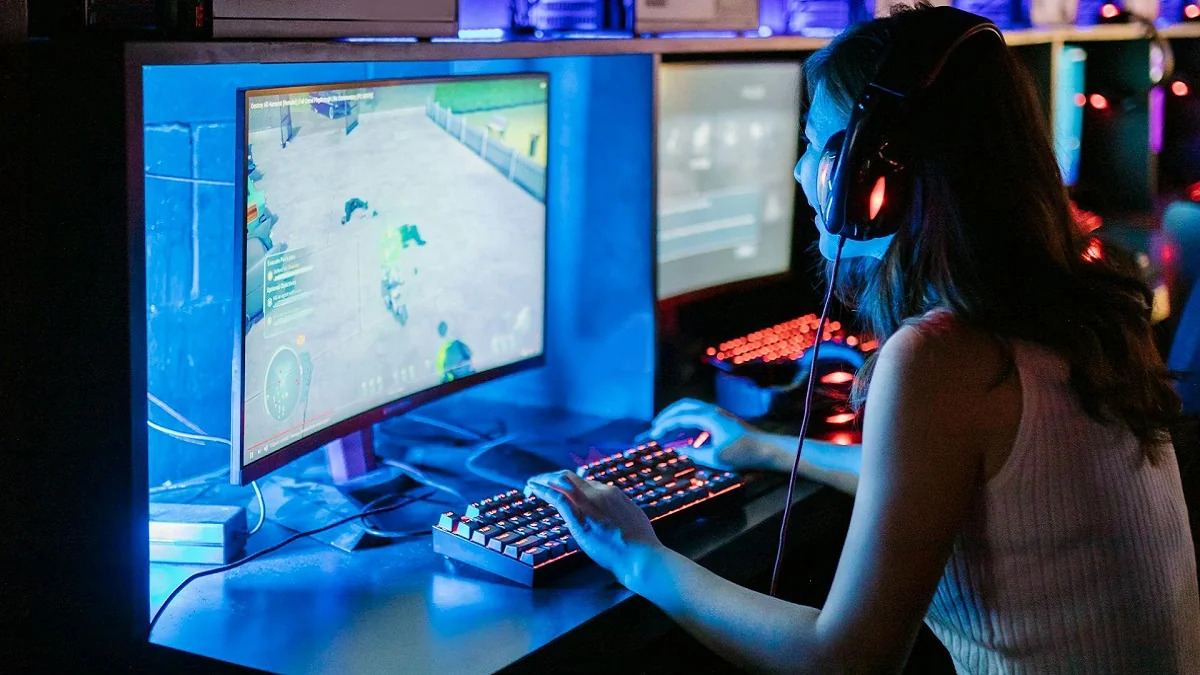 A photo of a young woman playing a game on a brightly lit PC.