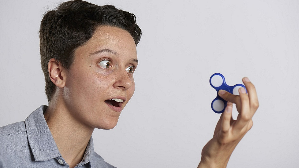 A photo of a caucasian boy with dark hair looking fascinated at the blue fidget spinner in his hand.