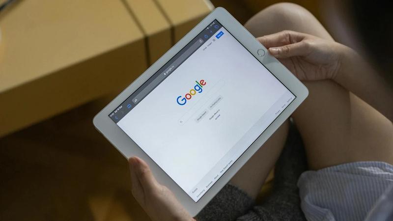A photo of a child's hands holding an iPad that's showing the Google homepage on-screen.