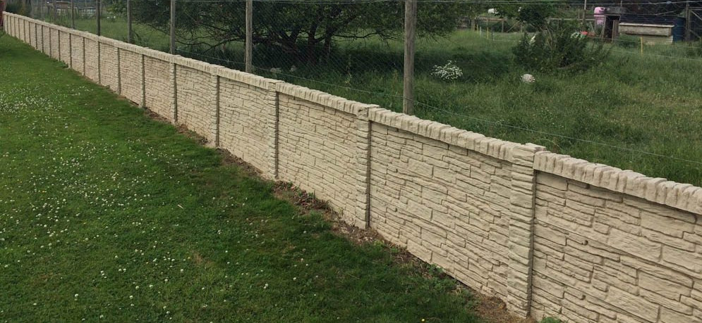 A photo of a tan, concrete wall running across a grass field.