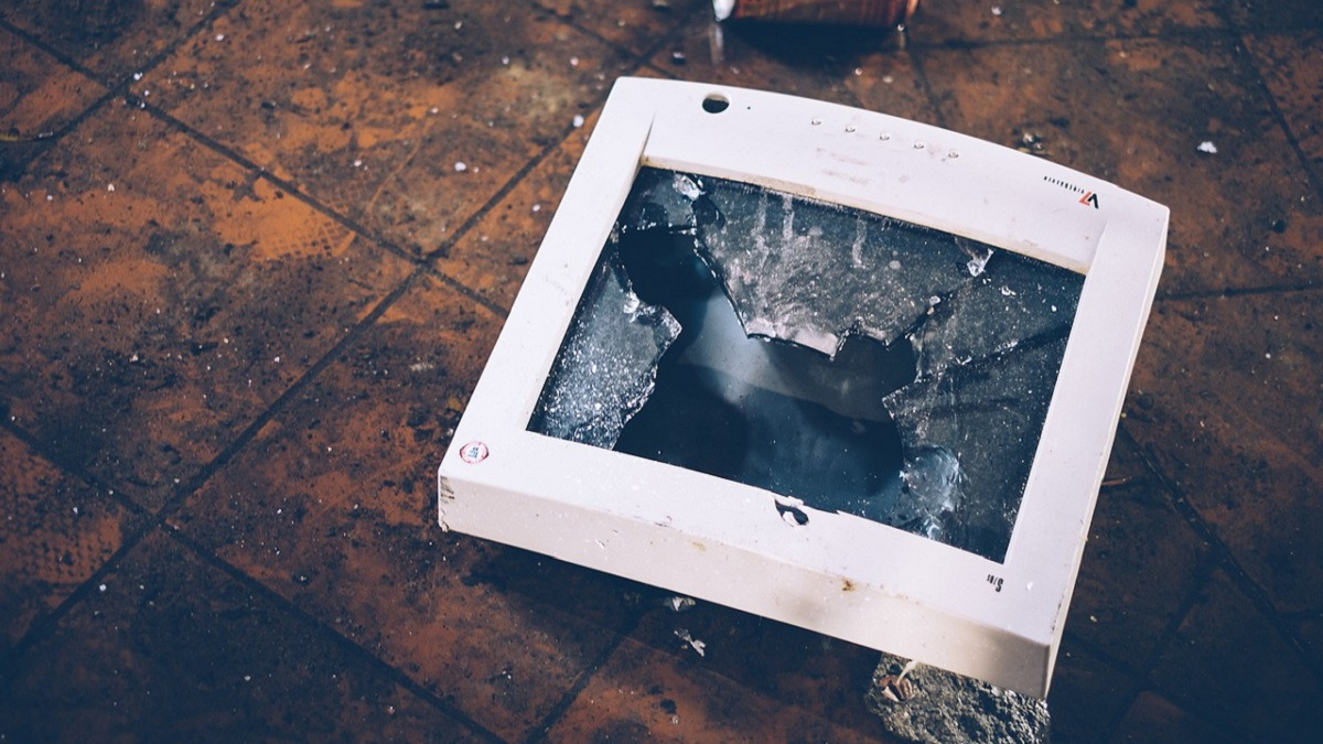 A photo of a broken computer monitor lying on a brown, tiled floor.