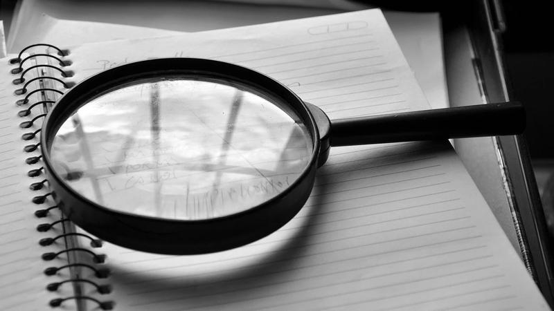 A black and white photo of a magnifying glass on top of a sheet of paper.