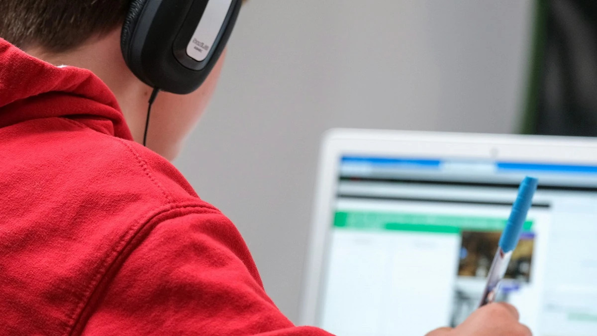 A photo of a young boy wearing red, concentrating on a laptop screen.