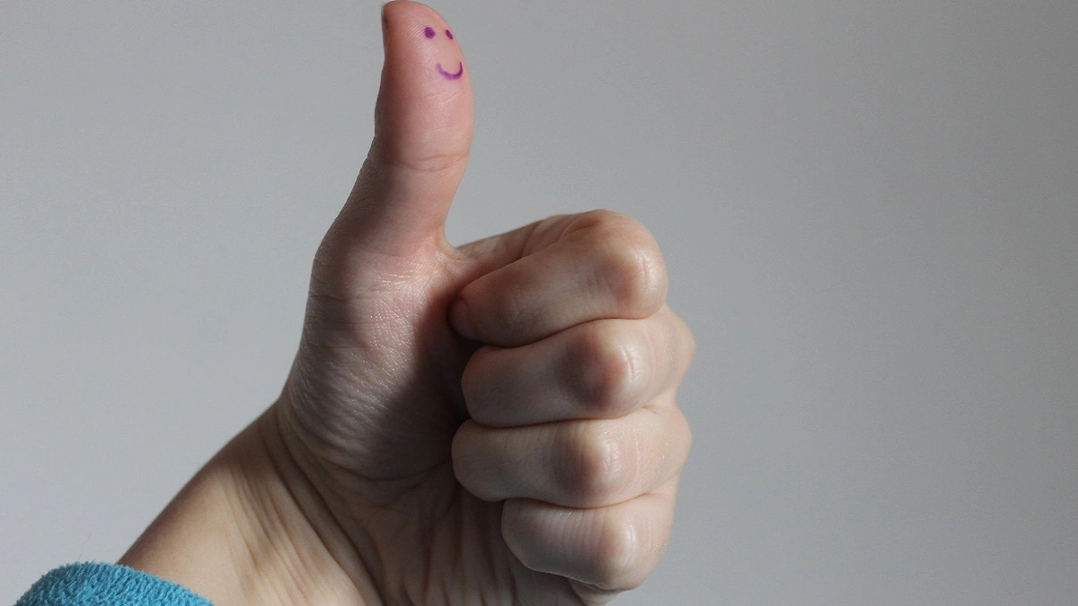 A photo of a hand doing a thumbs up, with a smiley face drawn on the thumb.